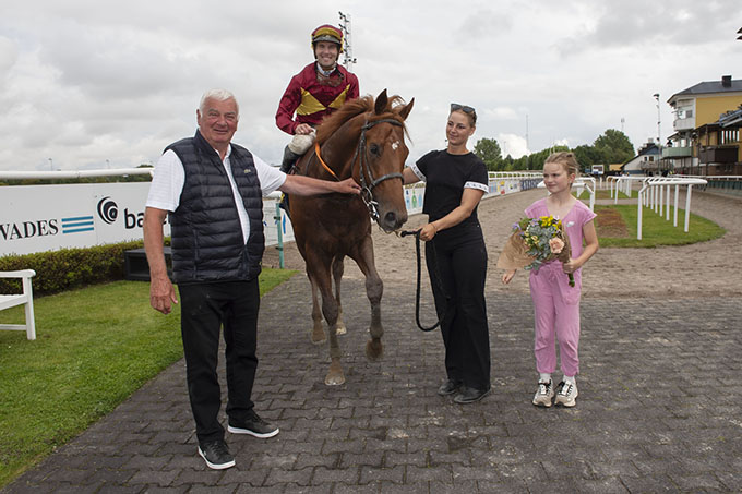 Great Wish (IRE) med jockey Oliver Wilson i vindercirklen på Jägersro 4. aug. 2024. Bent Olsens barnebarn Caroline holder vinderbuketten. 
	Mon ikke den kommer med hjem til fru Lone Kaj?  Foto: Stefan Olsson / Svensk Galopp